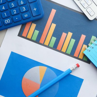 A piece of paper with financial planning charts with a calculator, notebook and a pencil resting on top.