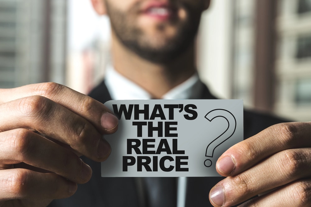 Business professional holding a card that reads "WHAT'S THE REAL PRICE?" symbolizing inquiries about bookkeeping costs and financial management.