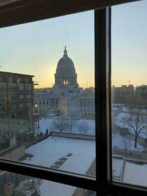 View of the Wisconsin State Capitol building in Madison at sunrise from an office window, with snow-covered rooftops in the foreground