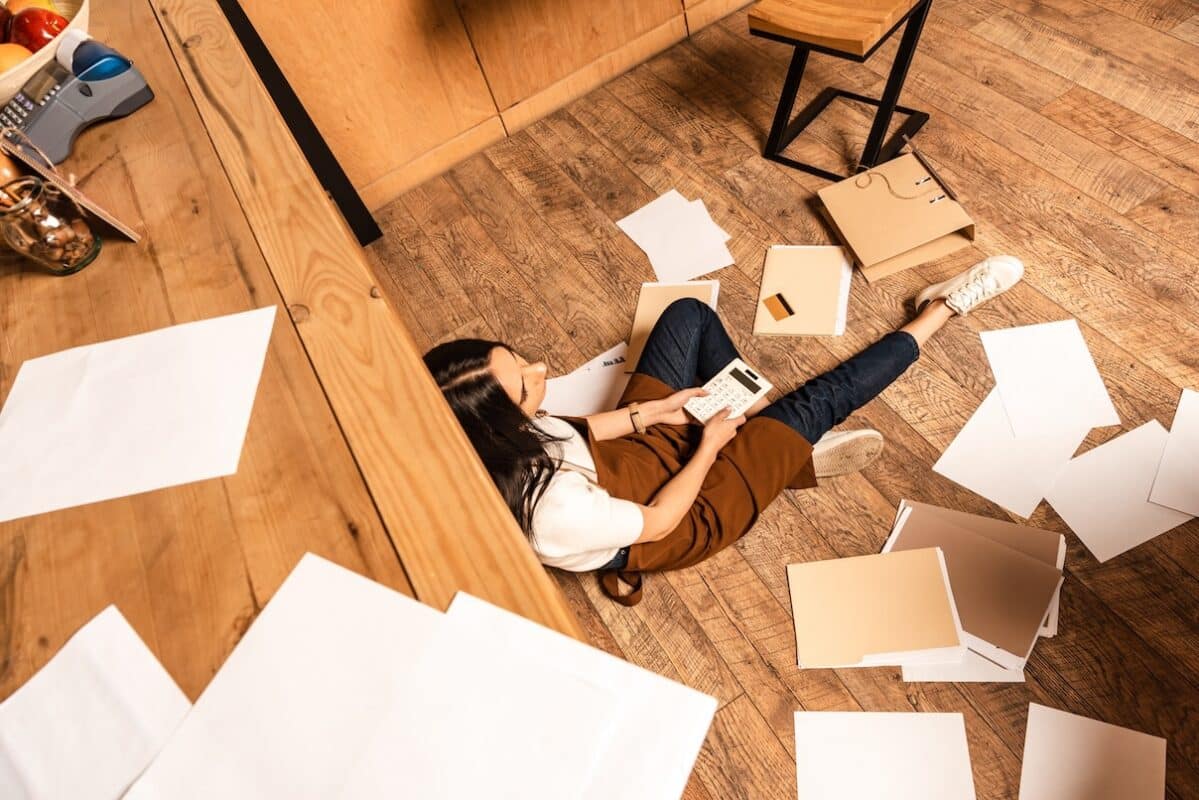 Business owner sitting on the floor surrounded by scattered papers and documents, trying to figure out bookkeeping cleanup costs